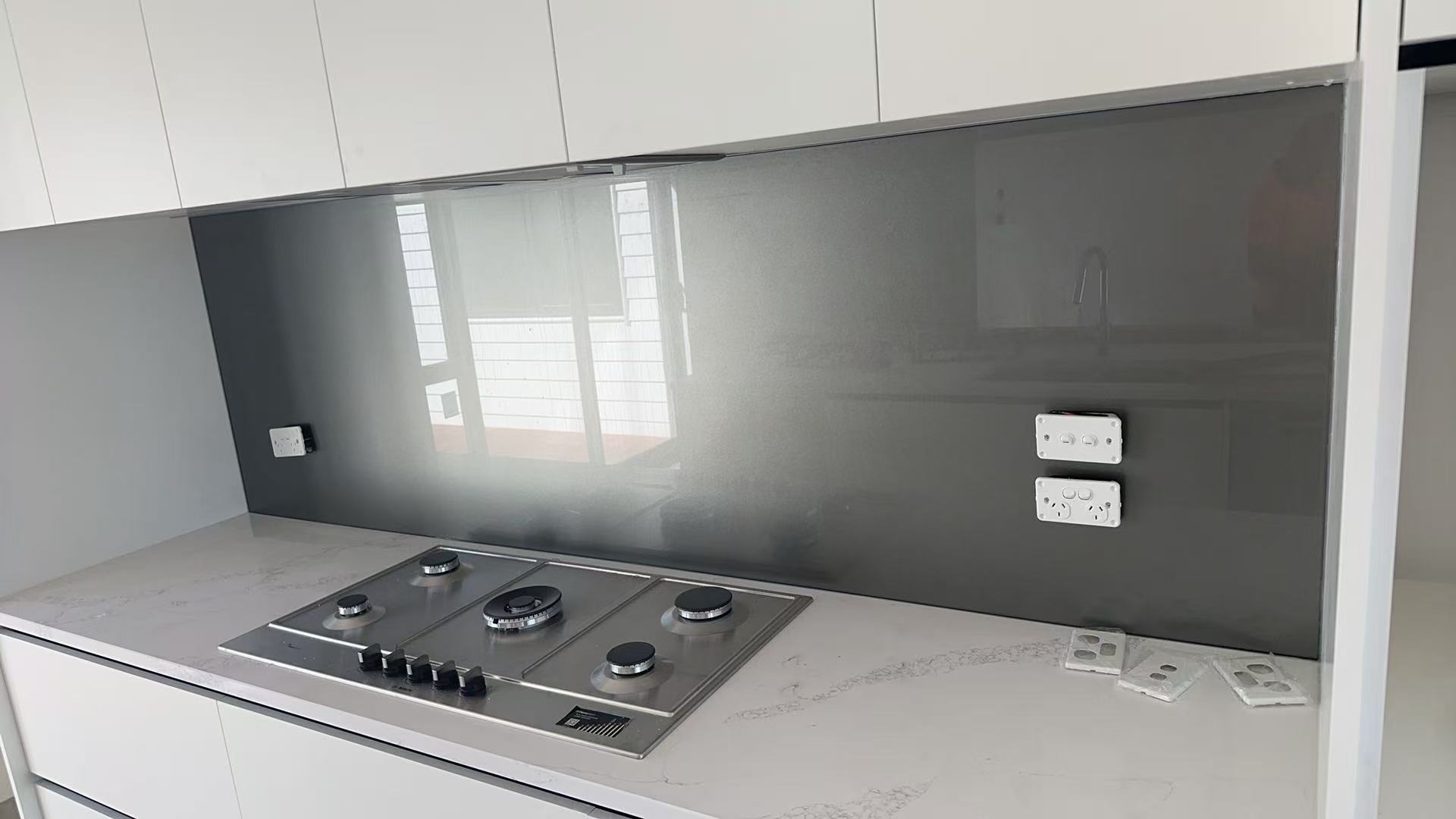 Smoked reflective glass splashback fitted behind a kitchen cooktop